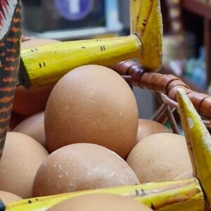 Cesta de mimbre con huevos marrones y detalle decorativo de madera pintada, sobre estantería de supermercado.